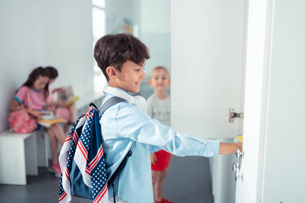 Handsome schoolboy wearing backpack standing near locker - Foto, Imagen