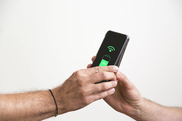 Two hands holding black smart phones while they are wireless charging. - Foto, imagen