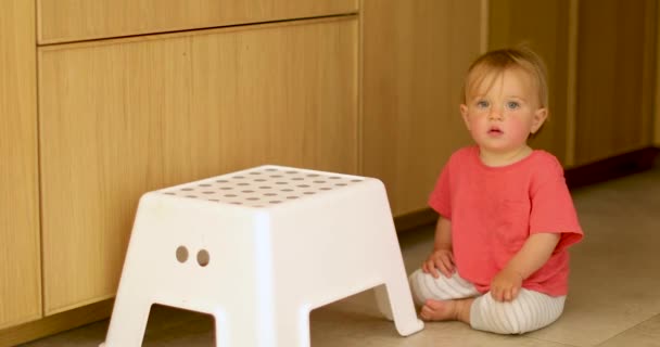 Αξιολάτρευτο παιδί κάθεται στο πάτωμα με λευκή καρέκλα - Πλάνα, βίντεο