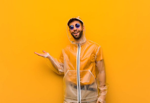 Fiatal férfi visel egy eső kabátot gazdaság valamit kézzel - Fotó, kép