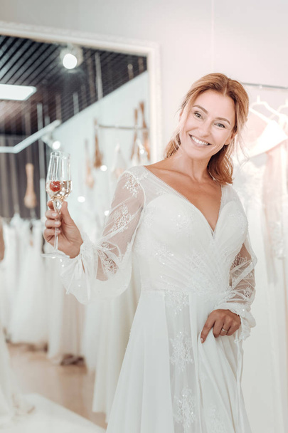Beautiful woman drinking champagne and trying on wedding dress. - Fotó, kép
