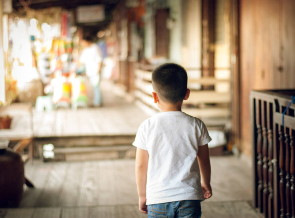 Το παιδί που φοράει φούτερ πάνω από απομονωμένο φόντο περπατάει ανάποδα κοιτάζοντας μακριά. Προσπαθεί να βρει το μέρος και δεν μπορούσε να το βρεί. Θολή υπαίθρια αγορά φόντο - Φωτογραφία, εικόνα