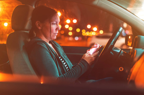 Vrouw texting op mobiele telefoon in auto 's nachts - Foto, afbeelding