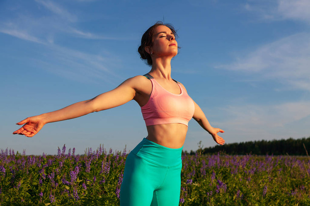 Sporty woman breathing clean and fresh air in the green field with blue sky behind - Photo, Image