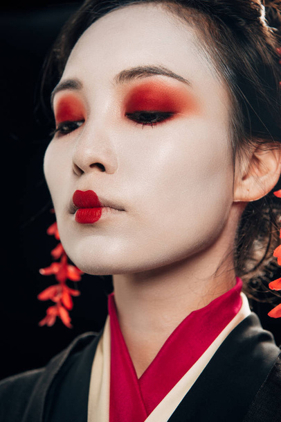 vista a basso angolo di bella geisha con ombretto rosso e labbra isolate sul nero
 - Foto, immagini