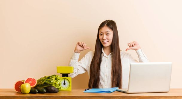 Young nutritionist chinese woman working with her laptop feels proud and self confident, example to follow. - Foto, Imagen