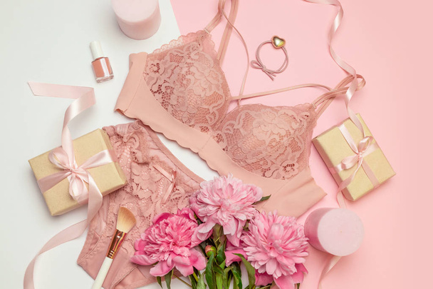 Female elegant pink lace bra and panties, pink candles, hair tie, a bouquet of beautiful peonies, nail polish, jewelry, top view - Foto, immagini