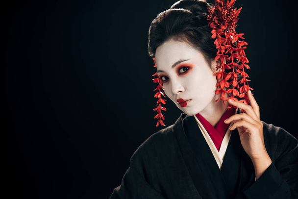 beautiful geisha in black and red kimono and flowers in hair isolated on black with copy space - Photo, Image