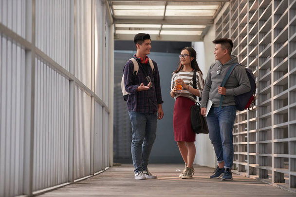 Uśmiechnięty Asian Engineering studenci chodzenie w kolegium korytarz i omawianie News - Zdjęcie, obraz