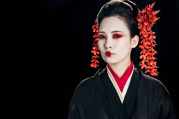 serious geisha in black and red kimono and flowers in hair isolated on black - Fotó, kép