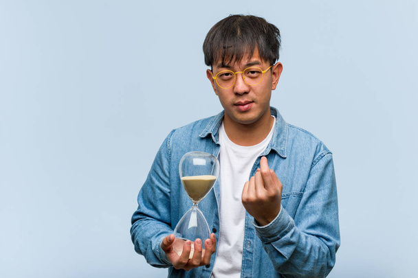 Młody chiński człowiek trzyma zegar piasku zapraszając przyjść - Zdjęcie, obraz