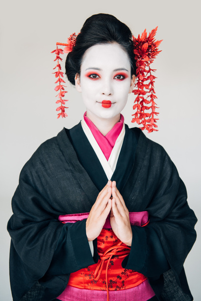 glimlachend mooi Geisha in zwarte kimono met groet handen geïsoleerd op wit - Foto, afbeelding