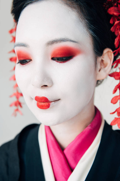 Widok z bliska uśmiechnięta piękna gejsza w czarnym kimono z czerwonymi kwiatami we włosach na białym tle - Zdjęcie, obraz