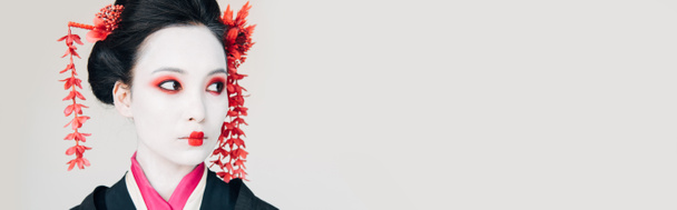 bela gueixa em quimono preto com flores vermelhas no cabelo olhando para longe isolado em branco, tiro panorâmico
 - Foto, Imagem