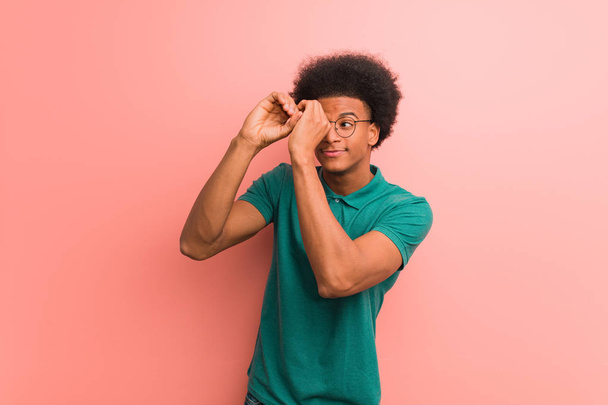 Giovane uomo afroamericano su un muro rosa che fa il gesto di un cannocchiale
 - Foto, immagini