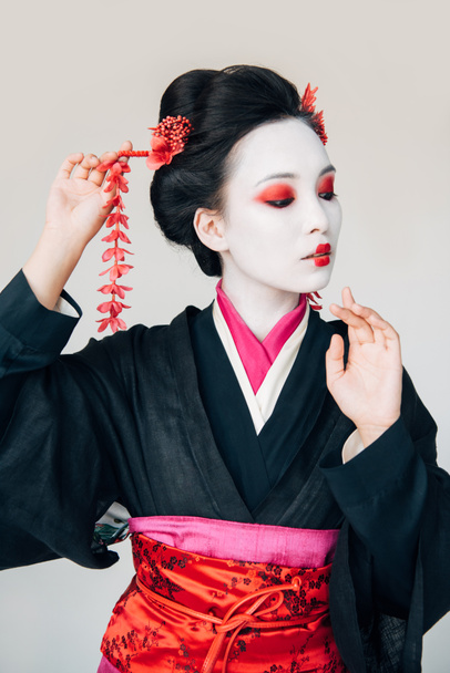 beautiful geisha in black kimono with red flowers in hair gesturing isolated on white - Photo, Image