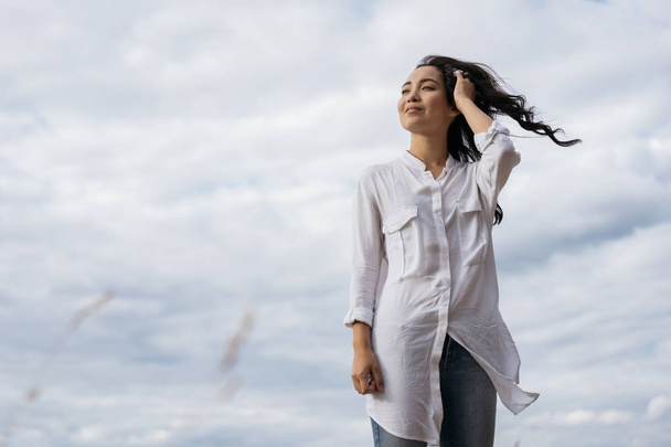 Portrait of cheerful asian woman walking in field, breathing fresh air. Happy Korean girl looking for inspiration, enjoying beautiful landscapes, windy weather and relaxing outdoor. Positive lifestyle, emotional moments concept  - Foto, Imagen
