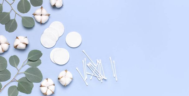 Cotton Cosmetic Makeup Removers Tampons. Spa concept. Flat lay background with cotton flowers, cotton pads, eared sticks, fresh eucalyptus twigs. Hygienic sanitary swabs on blue background Top view - Photo, Image
