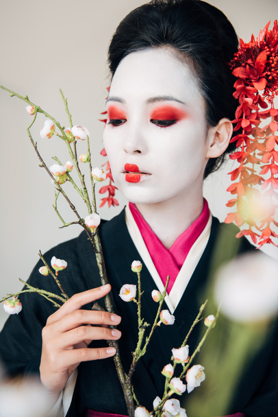 selective focus of tree branches and beautiful geisha with red and white makeup isolated on white - Foto, Imagem