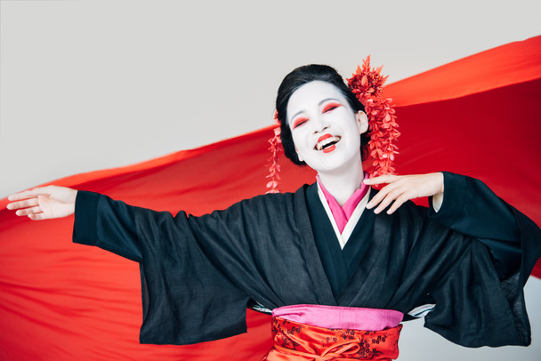 happy beautiful geisha in black kimono with red cloth on background isolated on white - Foto, imagen