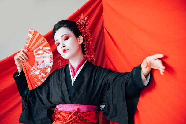belle geisha en kimono noir avec ventilateur à main et tissu rouge sur fond dansant isolé sur blanc
 - Photo, image