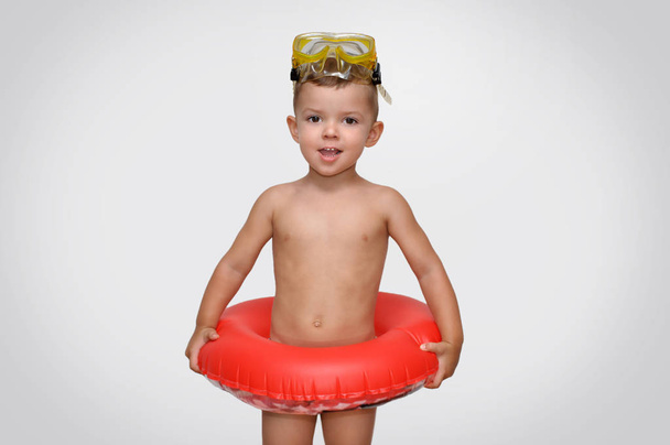 Netter kleiner Junge in gestreifter Badehose mit rotem aufblasbarem Ring und Taucherbrille - Foto, Bild
