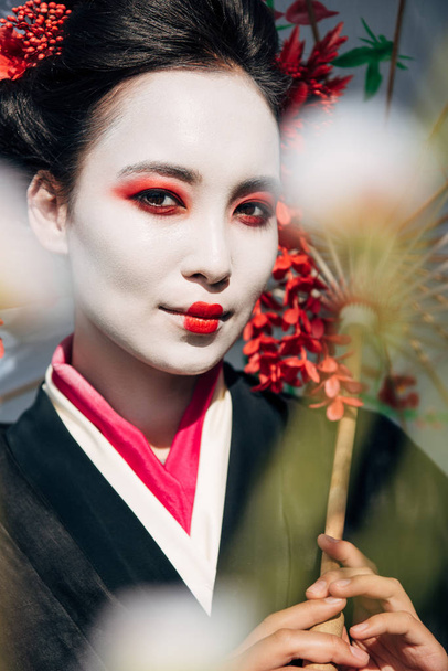 foyer sélectif de branches d'arbres et belle geisha souriante avec parapluie au soleil
 - Photo, image