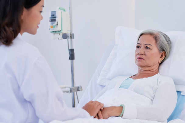 junge Krankenschwester erzählt einer fast weinenden Seniorin schlechte Nachrichten - Foto, Bild