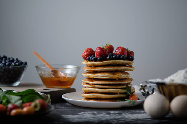 Turm von Pfannkuchen mit Honig und Beeren. Pfannkuchen zum Frühstück. morgendliches Stillleben. Pfannkuchen mit Erdbeeren und Blaubeeren. - Foto, Bild
