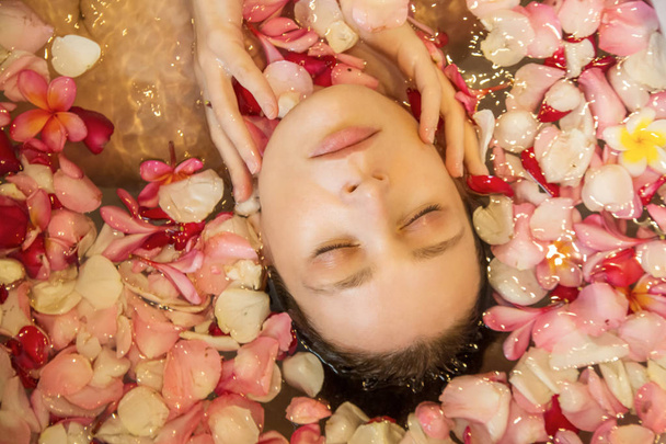 Retrato de bela jovem na banheira cheia de pétalas de frangipani, aparência natural, pele nua sem maquiagem
 - Foto, Imagem