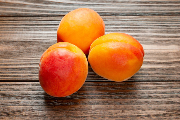 Ruddy apricots on a wooden background. Top view of three fresh juicy apricots piled on a wooden table.  - Photo, Image