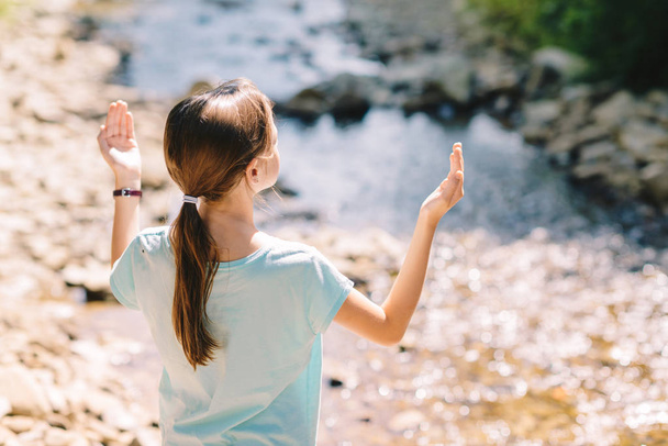Young girl raises her arms praying on the banks of a mountain st - Foto, Bild