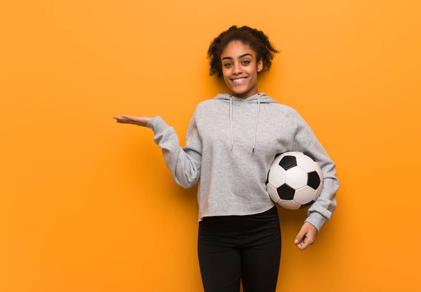 Молодая темнокожая женщина держит что-то за руку. Холдинг футбольный мяч
. - Фото, изображение