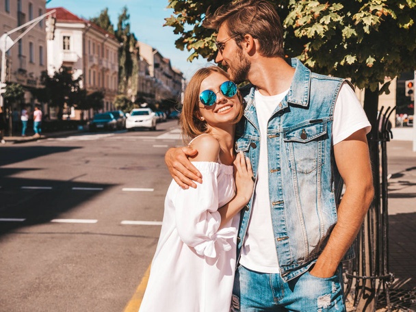 Smiling beautiful girl and her handsome boyfriend. Woman in casual summer dress and man in jeans clothes. Happy cheerful family. Female having fun on the street background.Hugging couple in sunglasses - Fotografie, Obrázek