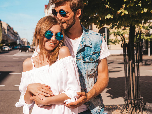 Smiling beautiful girl and her handsome boyfriend. Woman in casual summer dress and man in jeans clothes. Happy cheerful family. Female having fun on the street background.Hugging couple in sunglasses - Foto, Imagem