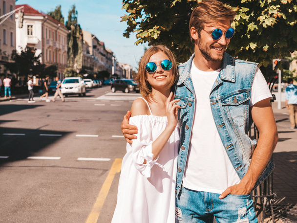 Smiling beautiful girl and her handsome boyfriend. Woman in casual summer dress and man in jeans clothes. Happy cheerful family. Female having fun on the street background.Hugging couple in sunglasses - Foto, afbeelding