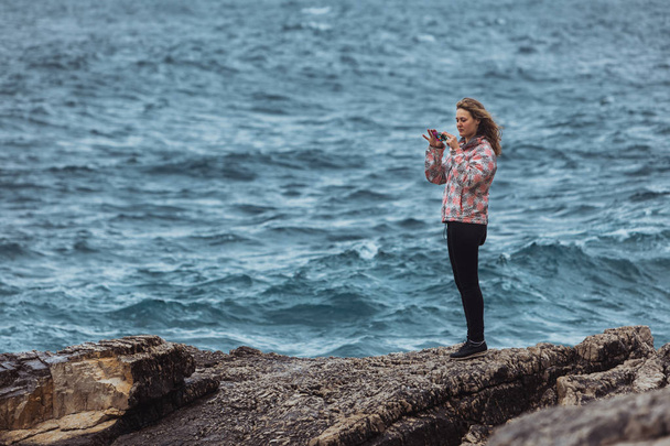 deniz kenarında paltolu genç kadın fırtınalı denize bakıyor - Fotoğraf, Görsel
