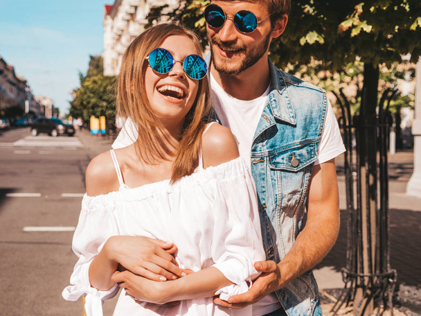 Smiling beautiful girl and her handsome boyfriend. Woman in casual summer dress and man in jeans clothes. Happy cheerful family. Female having fun on the street background.Hugging couple in sunglasses - Photo, Image