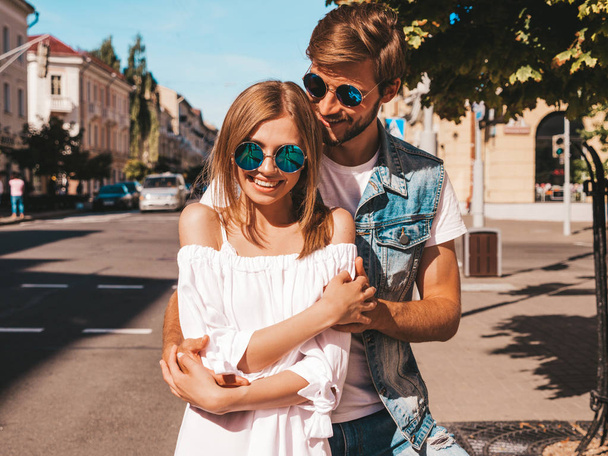 Smiling beautiful girl and her handsome boyfriend. Woman in casual summer dress and man in jeans clothes. Happy cheerful family. Female having fun on the street background.Hugging couple in sunglasses - Foto, imagen