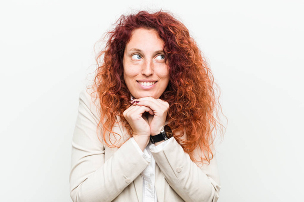Young natural redhead business woman isolated against white background keeps hands under chin, is looking happily aside. - Photo, Image