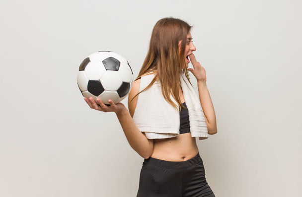 Young fitness russian woman whispering gossip undertone. Holding a soccer ball. - Photo, Image
