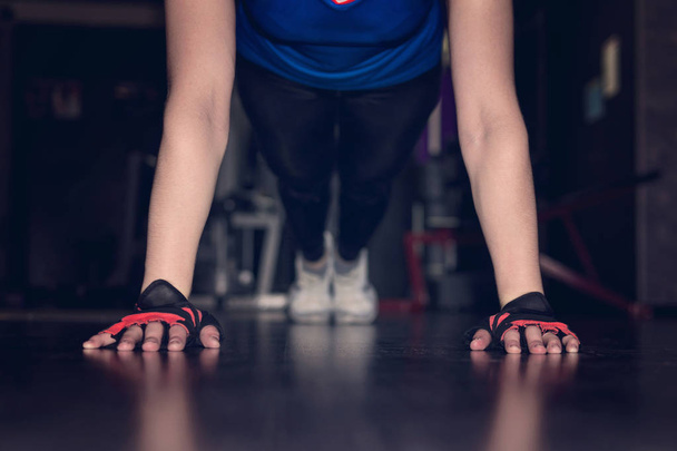 Close-up vrouw hand doen push-ups oefening in een sportschool in de nacht. concept gymnastiek, handen in zwarte handschoenen zonder vingers close-up op de vloer. - Foto, afbeelding