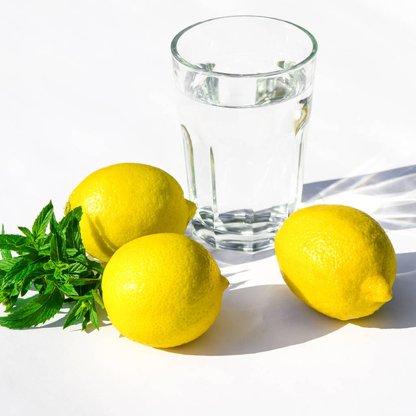 Lemons, fresh green mint and a glass glass with water on a white background - Фото, изображение