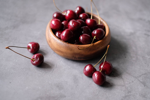 Dark red cherries in a bowl on wooden and gray  background  - Photo, image