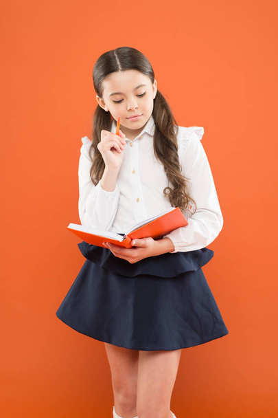 small girl in school uniform. get information form book. back to school. little child concentrated on work. reading lesson. schoolgirl writing notes on orange background. prepare for reading exams - Zdjęcie, obraz