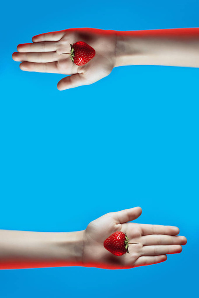 colagem de morangos suculentos brilhantes na mão no fundo azul
 - Foto, Imagem