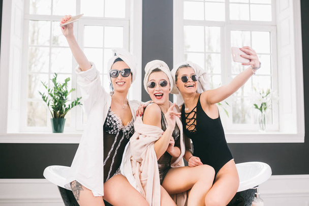 Picture showing group of happy friends in spa. girls with towels on heads having fun and taking selfie at home. Friendship, cosmetic, slumber party concept. Hen party with a bride in hotel - Photo, Image