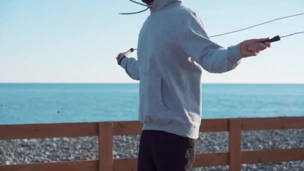 Sportsman is jumping rope in sunny day near sea - Footage, Video