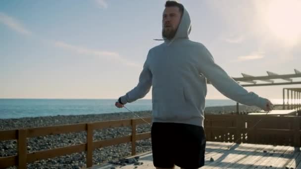 Homem forte está pulando corda rápido perto da praia de seixos na manhã de verão
 - Filmagem, Vídeo