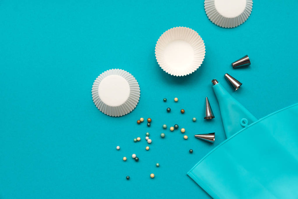 Pastry bag, cupcake cases and sugar sprinkling on blue pastel background. Top view. Flat lay. Copy space. Baking utensils for cooking dessert - 写真・画像
